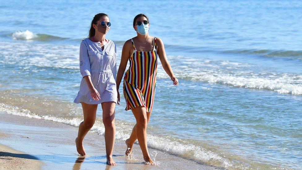 Women in masks walking along the beach