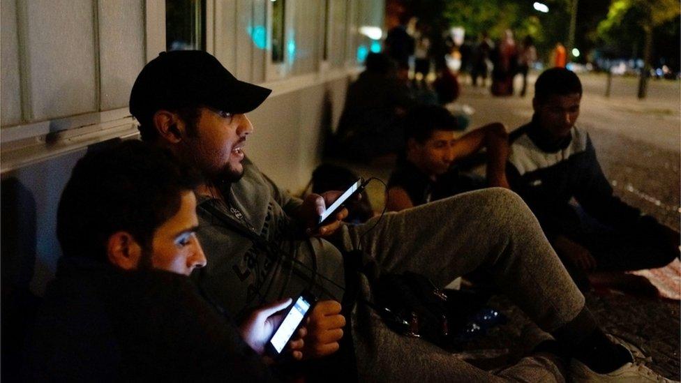 Two refugees from Syria chat on their smartphones with their relatives in Syria as they wait in front of the the Central Registration Office for Asylum Seekers in Berlin