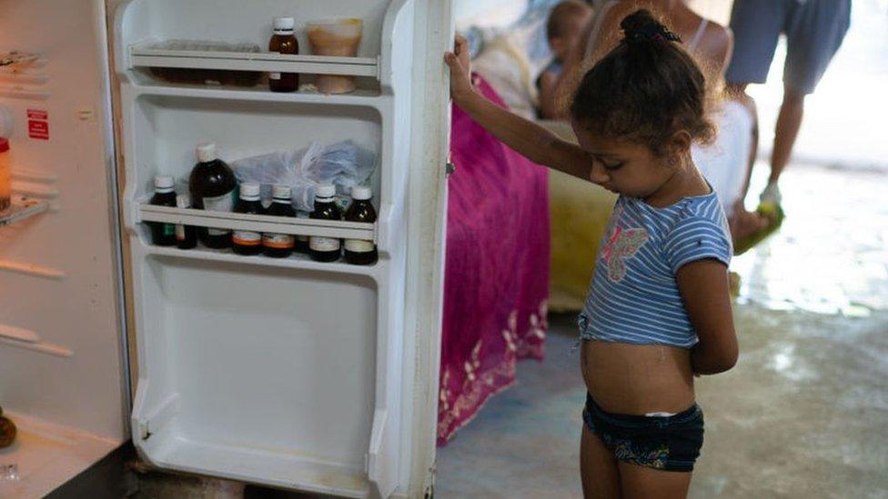 Laurent Alemany, aged 4, wears a blue and white stripy top and is holding the door to the fridge open while she looks for food