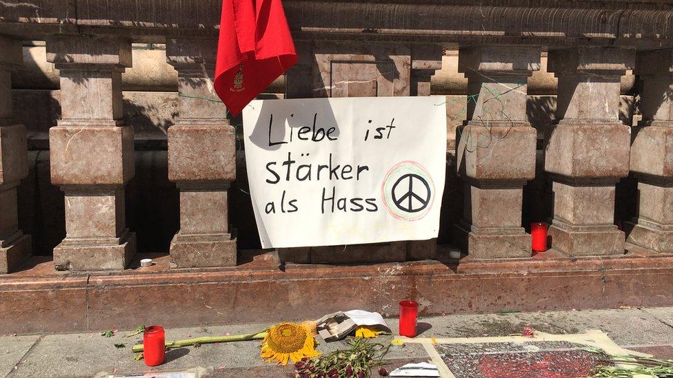 Sign reading "Love is stronger than hate" in German, above candles and flowers, in central Munich