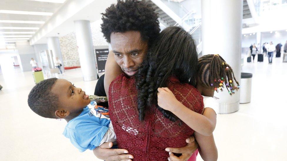 Olympic silver medallist Feyisa Lilesa, rear, of Ethiopia, hugs his wife Iftu Mulia, his daughter Soko, right, five, and son Sora, left, three, while picking up his family at Miami International Airport, Tuesday 14 February 2017, in Miami, the US