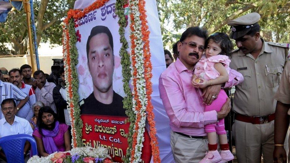 A relative carries Vismaya, daughter of India"s National Security Guard commando Niranjan Kumar, portrait seen, who was among those killed in the attack on the Pathankot air force base, next to his coffin placed for public viewing, in Bangalore, India, Monday, Jan. 4, 2016.