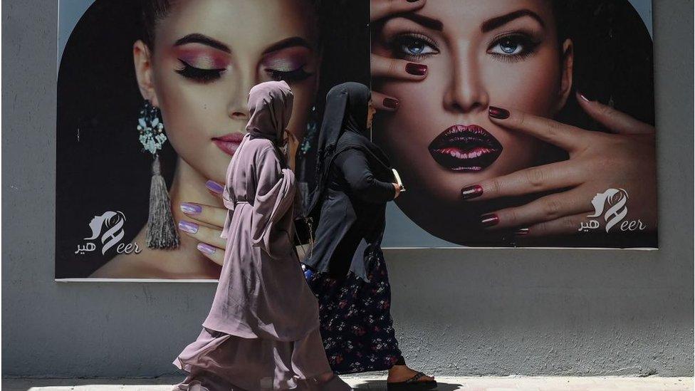 Women walking past a billboard for a beauty salon in Kabul in August 2021