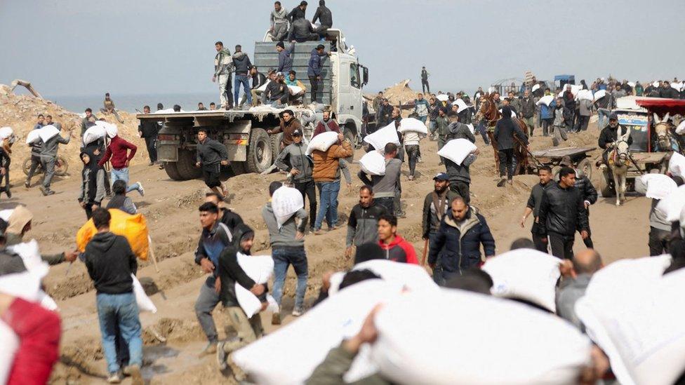 Palestinians carry bags of flour taken from an aid lorry near an Israeli military checkpoint in Gaza City, in the north of the Gaza Strip (19 February 2024)