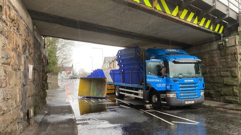 Lorry sat under the bridge as the skips it was carrying lie on the road