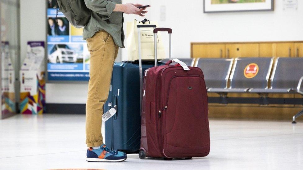 An image of a person standing next to two large suitcases in an airport