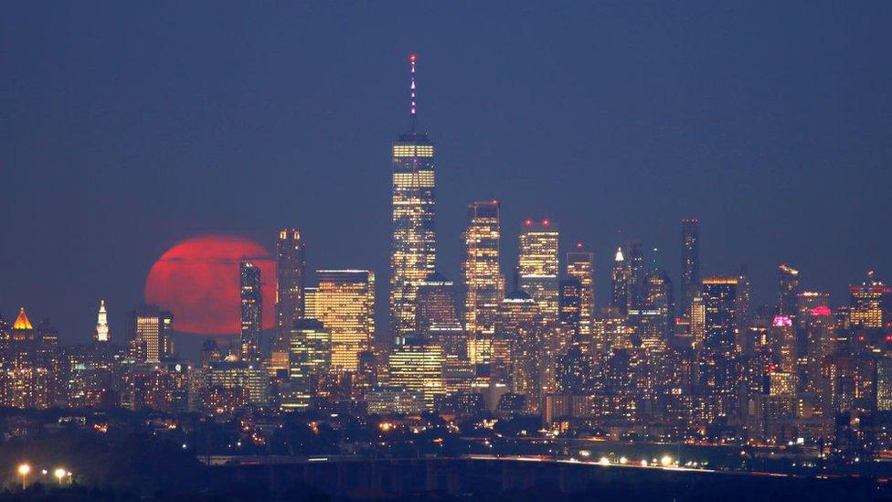 Here the buck moon rises behind lower Manhattan and One World Trade Center in New York City.