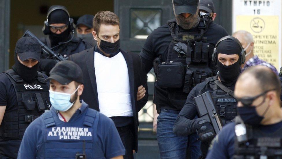 Babis Anagnostopoulos being led out of court, surrounded by heavily armed police