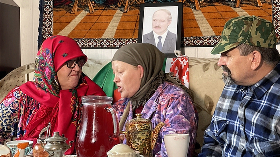 Anna Fedoronok and co-performers sit in traditional Belarusian clothes on a sofa