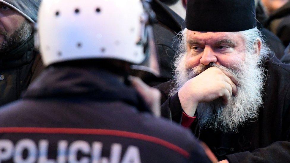 Serbian Orthodox Church clergy and believers stand in front of police near the parliament on 26 December