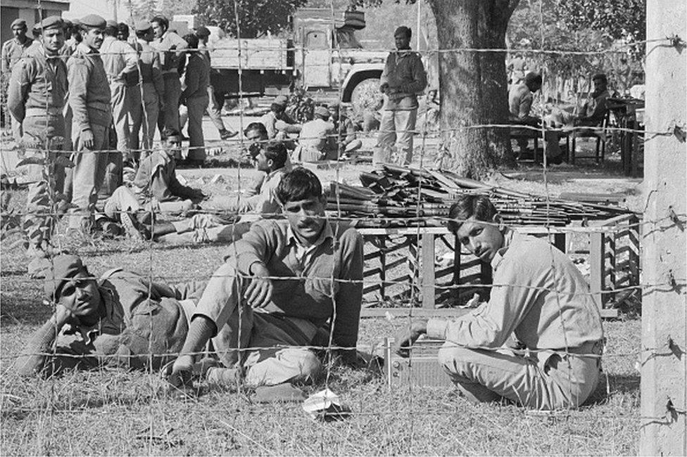 Captured Pakistani soldiers sit behind a barbed wire fence at a prison camp here.