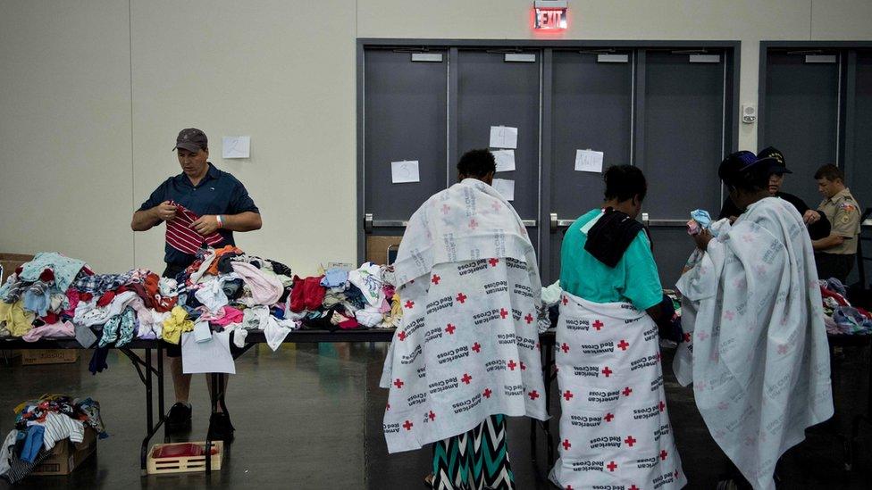 Flood victims in Red Cross blankets look for clothing at a shelter in the George R. Brown Convention Center