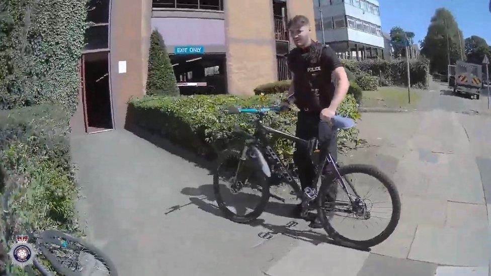 Police officer standing with a bicycle outside a multi-storey car park