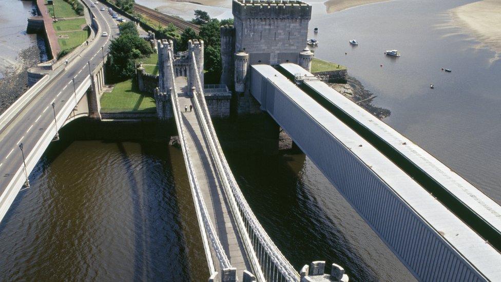 Aerial photo showing three bridges across the muddy coloured River Conwy - the road bridge is the one on the left