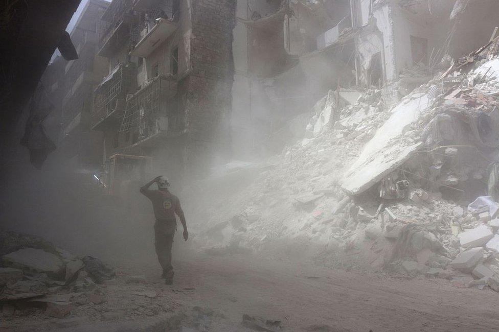 A White Helmet walks past the remains of a blasted building in Aleppo (2016)