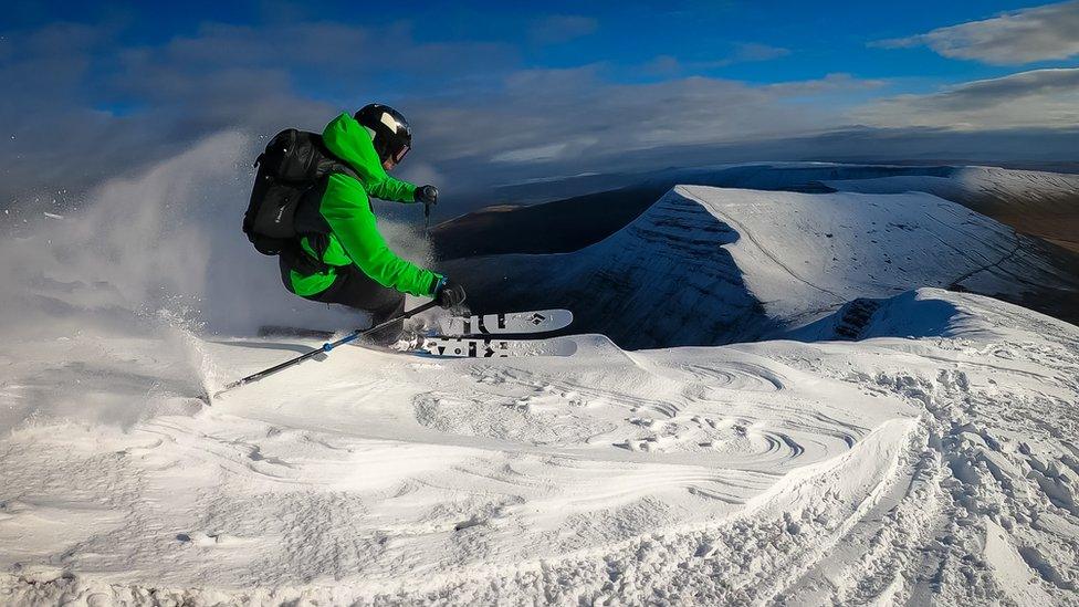 Chris skiing fast through the snow with a snow covered mountain peak in the distance