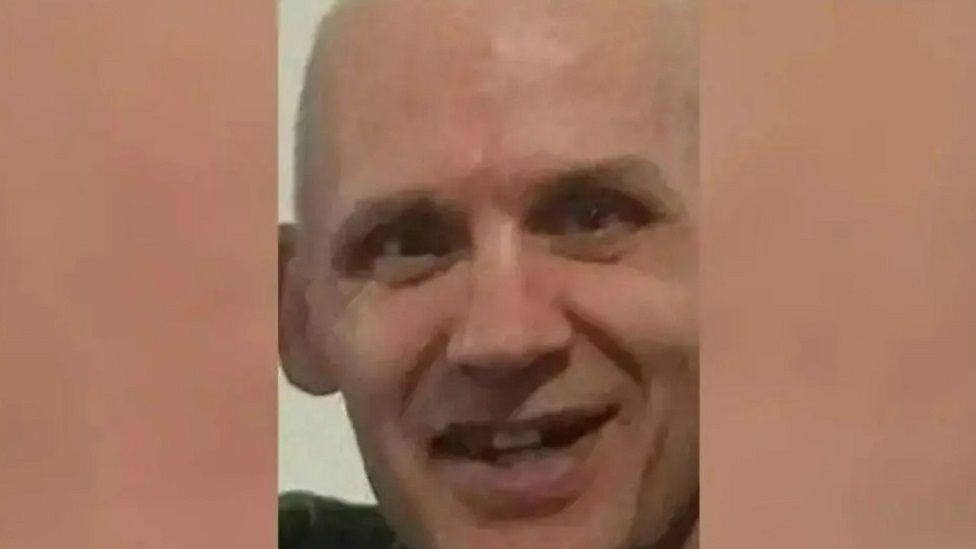 Kevin Ryan smiling at the camera, with his mouth open and teeth showing. He does not appear to have hair.