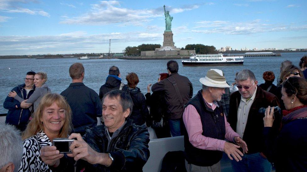 A group of tourists take and pose for photographs as they pass near the Statue of Liberty