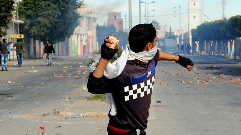 A young man throwing a stone in a street filled with smoke