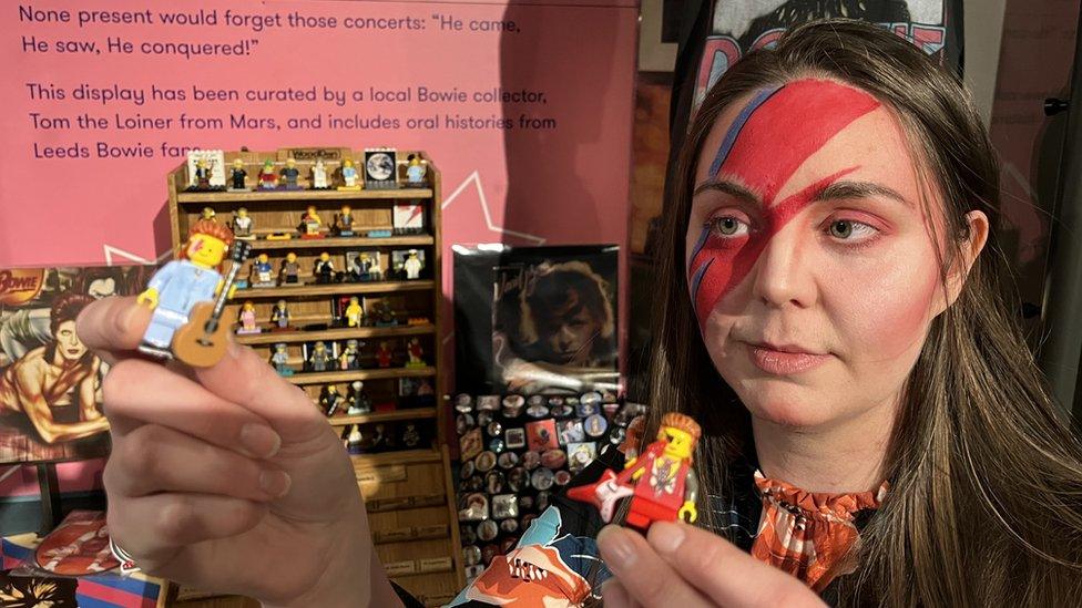 Woman with Ziggy Stardust makeup holding up David Bowie-themed Lego figurines