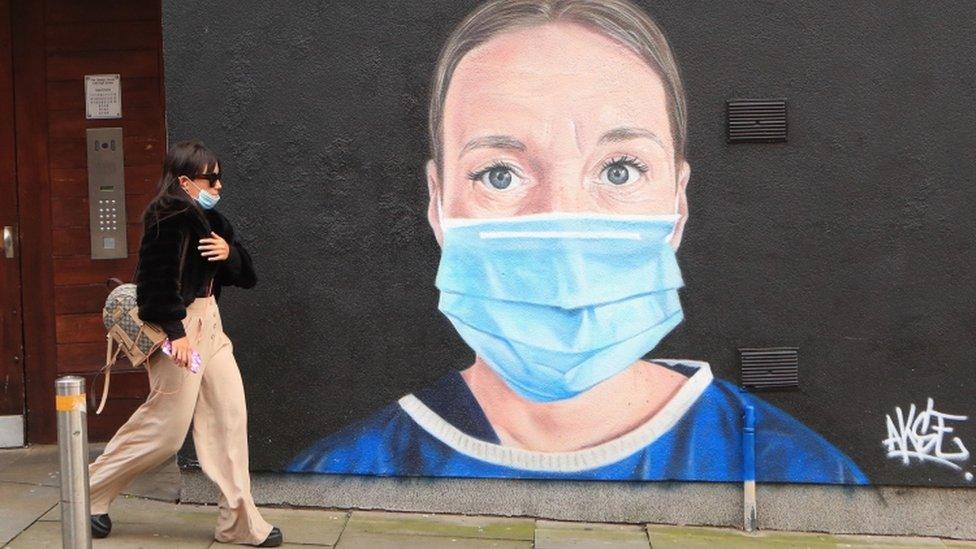 A woman walks past a mural of an NHS worker in central Manchester