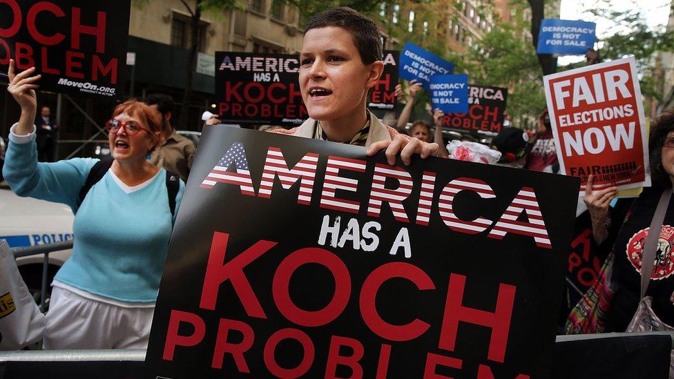 A woman holds up a sign reading "America has a Koch problem"