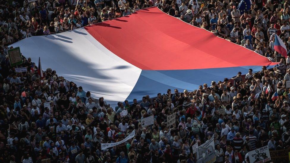 People carry a large Czech national flag as thousands of demonstrators gather to protest against Czech Prime Minister Andrej Babis on 4 June