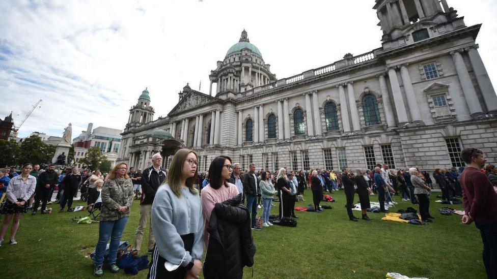 Large group of people stand on grass, watching the Queen's funeral.