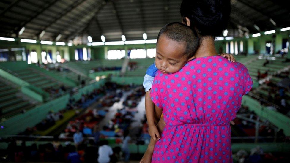 A boy is seen asleep on his mother's shoulder in a evacuee shelter inside a sports hall