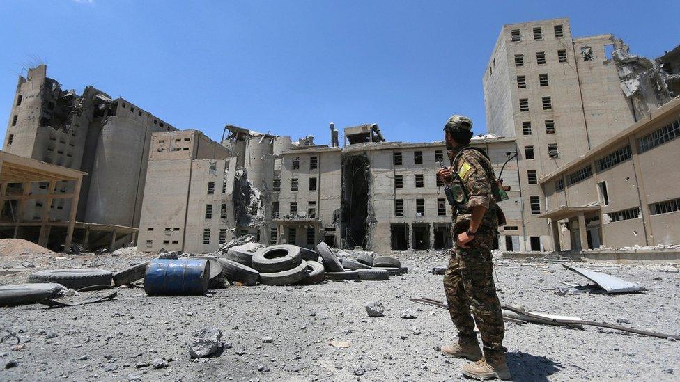 A Syria Democratic Forces (SDF) fighter stands near war-damaged silos and mills of Manbij (1 July 2016)