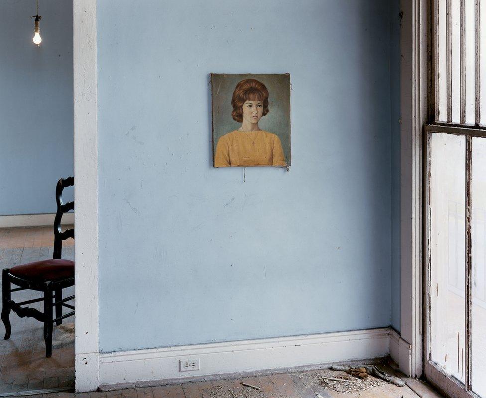 A blue wall with a portrait of a woman hanging on it.