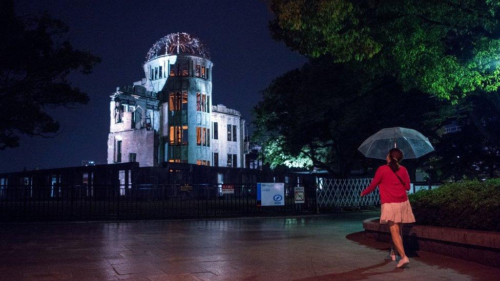 A pedestrian walking past the illuminated Atomic Bomb Done at night