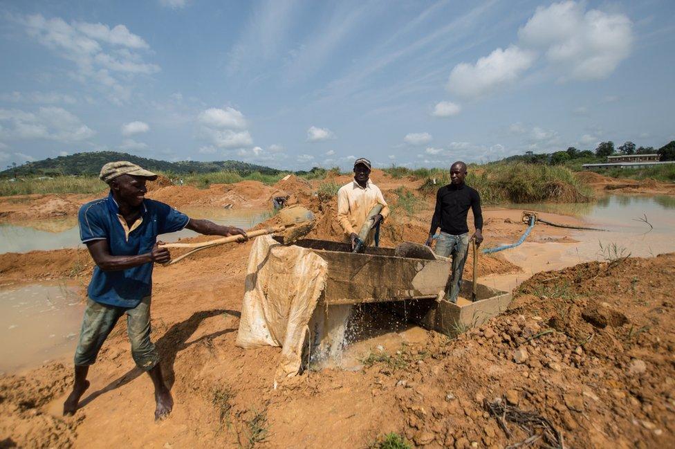 The men shovel dirt into a trough and then wash it with water