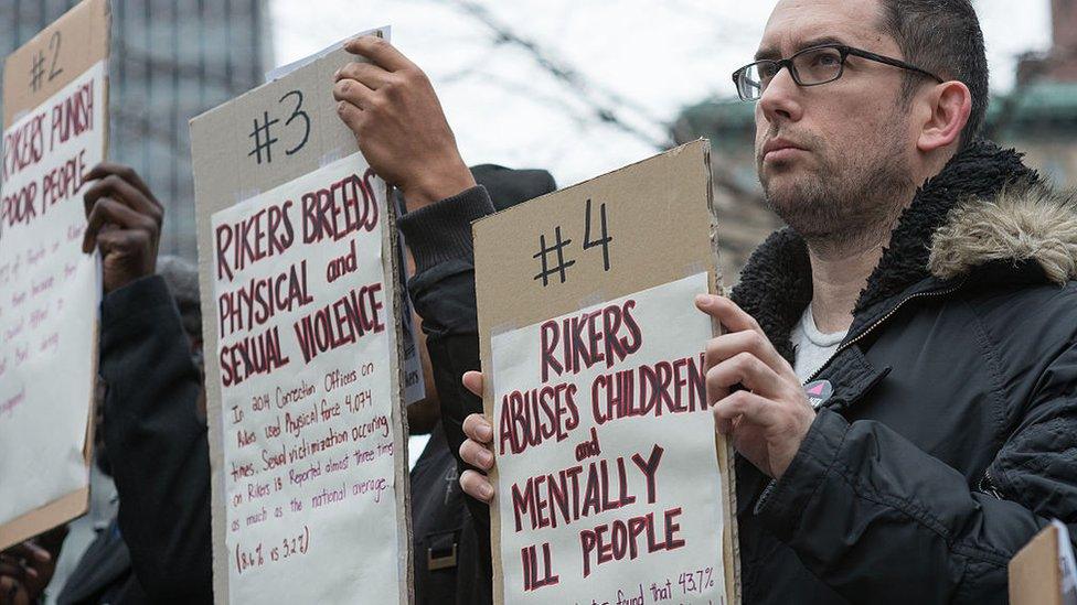 Protesters holding up signs stating reasons to shut down Rikers