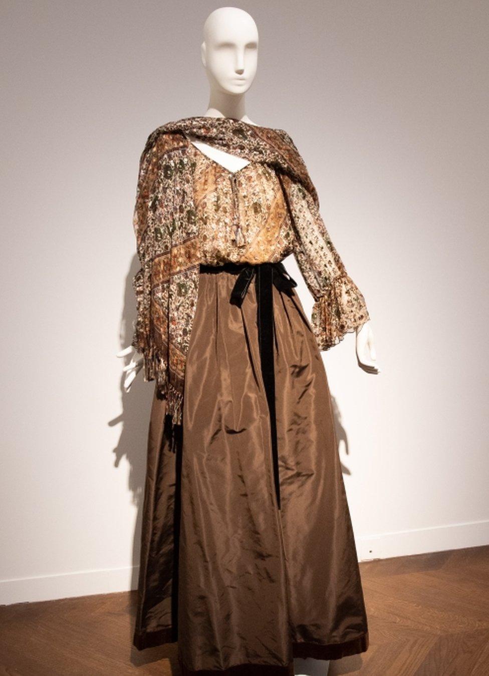 A long brown evening gown featuring a ribbon at the waist, and a wrap shawl