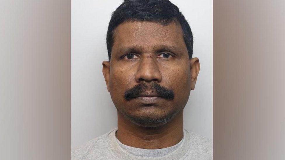 Mugshot of Saju Chelavalel. He has black hair, a moustache and is wearing a grey sweatshirt