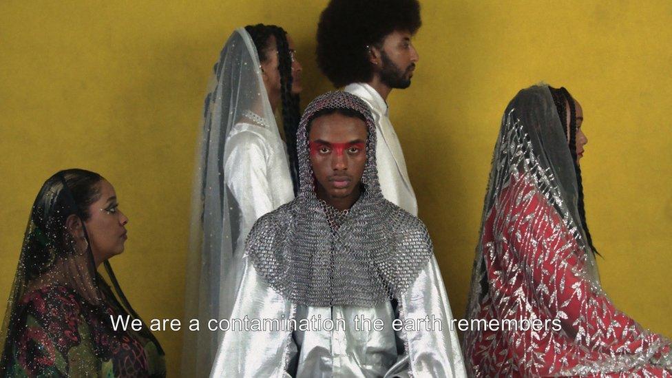 Still from Jama's film, featuring five people. One is staring directly at the camera whilst the caption reads "We are a contamination the earth remembers"