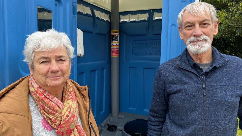 Dee and Bill Wells standing next to their portable toilet