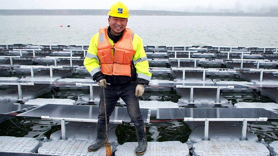 Wu Wenhui in yellow hard hat and orange life jacket standing on floating solar panels