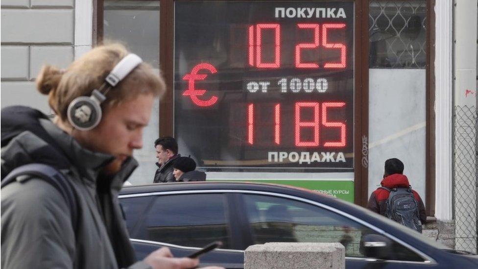 People walk in front of digital panel displaying the euro and US dollar currency rate at an exchange office in St. Petersburg, Russia, 28 February 2022.