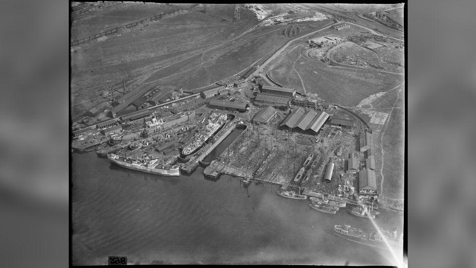 A black-and-white aerial shot of dockyards on a waterbody.