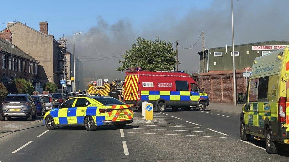 Emergency vehicles at the scene as smoke pours into the air