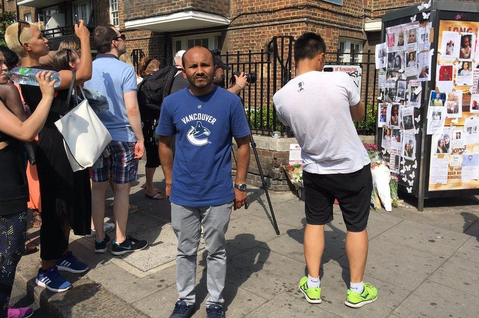 Nurul Islam in front of a crowd of people, many of whom are taking pictures of the memorials