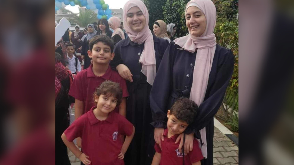 Three boys in red shirts, two girls in pink scarves and dark dresses