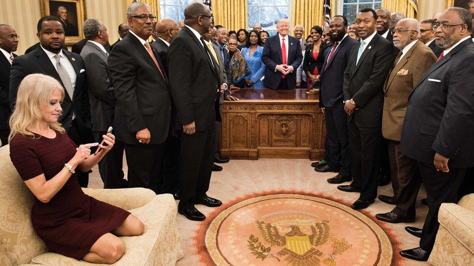 Kellyanne Conway checks her phone after taking a photo as US President Donald Trump and leaders of historically black universities and colleges in the Oval Office of the White House, 27 February 2017