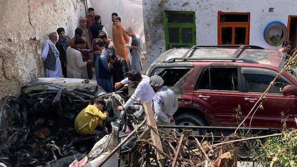 A photograph showing the destroyed car and damage around it