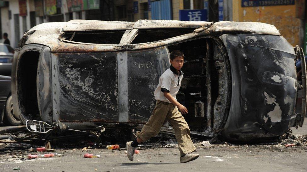 A boy runs in front of the burnt wreck of a car in a street in Urumqi in July 2009