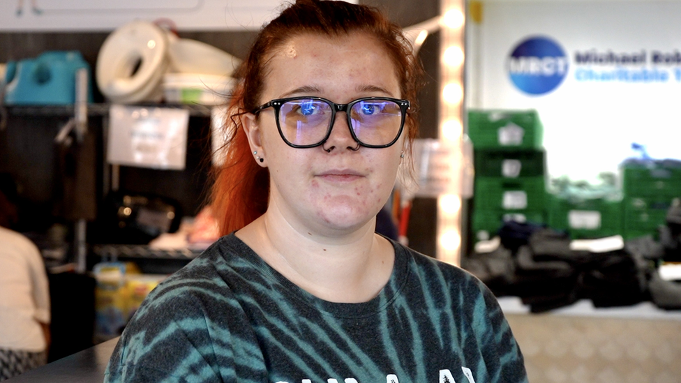 Ellie Marmon looking down the camera, standing in the uniform exchange shop.