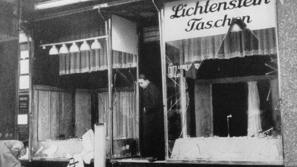 Jewish shop owner clears broken glass from shop front