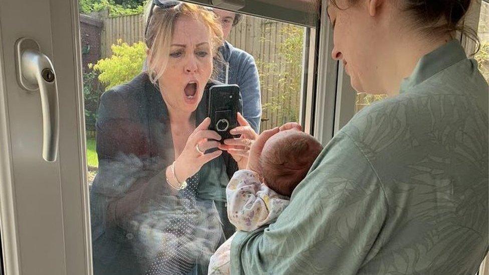 Woman looks overjoyed as she takes picture of baby through a window